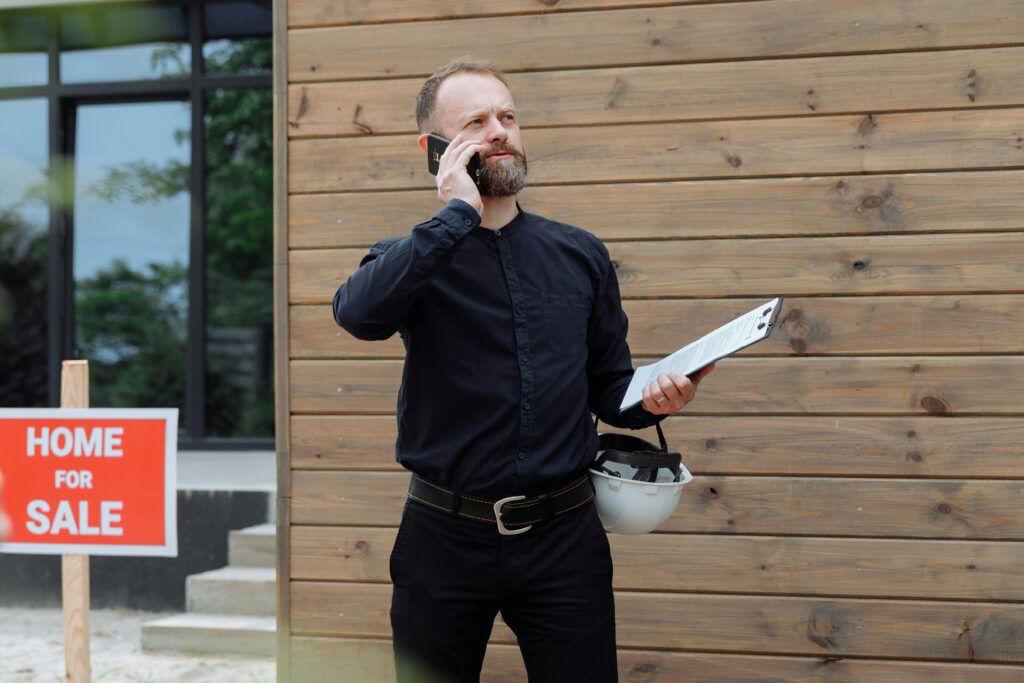 Real estate professional on a phone call near a home for sale sign